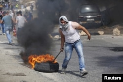 A Palestinian protester drags a burning tyre during clashes with Israeli troops in the West Bank city of Hebron, Oct. 18, 2015.