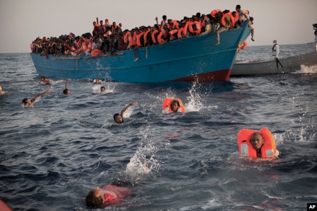 FILE - Migrants jump into the water from a crowded wooden boat as they are helped by members of an NGO during a rescue operation at the Mediterranean sea, about 13 miles north of Sabratha, Libya, Aug. 29, 2016.