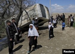Schoolgirls walk past a damaged mini-bus after it was hit by a bomb blast in the Bagrami district of Kabul, Afghanistan April 11, 2016.