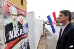 Bosnian Croat Pero Pervisic, 49, a friend of the late Slobodan Praljak, pays his respects in front of house where Praljak was born, in Capljina, Bosnia, Nov. 30, 2017. On the house are posters reading, "Our hero."