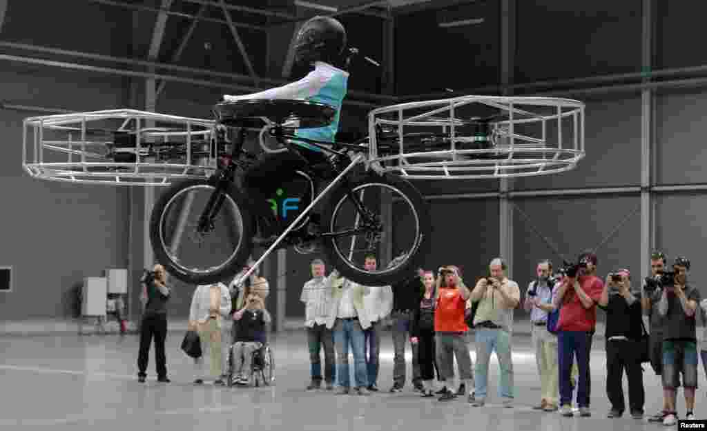 Journalists attend a presentation of a flying bicycle, carrying a dummy, at Letnany&#39;s fair hall in Prague, Czech Republic. The flying bicycle, which was created by Czech designers, is kept aloft by six electrically-powered propellers. 