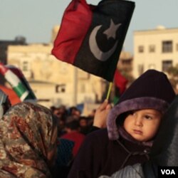 Seorang perempuan Libya menggendong bayinya dalam unjuk rasa anti-Gaddafi di Benghazi (22/3).