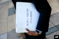 FILE - Omar Jadwat, director of the ACLU's Immigrants' Rights Project, carries court documents after a news conference outside a federal courthouse in Greenbelt, Md., Oct. 16, 2017, following a hearing regarding three lawsuits over the Trump administratio
