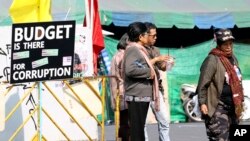 Thai anti-government protesters chat next to a protesting banner outside a makeshift camp where their colleagues were shot outside the Prime Minister's office of Government House, Saturday, Dec. 28, 2013 in Bangkok, Thailand.