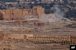 FILE - In this, April 14, 2016 file photo, Russian soldiers watch as smoke rises from a controlled land mine detonation inside the ancient town of Palmyra, Syria. An American heritage organization said the Russian military was constructing a new army base within the protected zone that holds the archaeological site listed by UNESCO as a world heritage site.