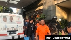 Para tersangka provokator demo berjalan ke mobil tahanan, usai konferensi pers di Mapolda Metro Jaya, Kamis (23/5) sore, sementara ambulans pembawa batu turut ditampilkan ke publik sebagai barang bukti. (VOA/Rio Tuasikal).