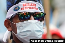 Seorang anggota serikat buruh mengenakan ikat kepala bertuliskan "batalkan UU Cipta Kerja" dalam demo memprotes perubahan aturan ketenagakerjaan di Jakarta, Senin, 25 November 2021. (Foto: Reuters)
