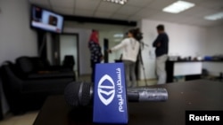 Journalists interview an employee as the logo of the Palestine Today TV station is seen following a raid by Israeli forces in the West Bank city of Ramallah, March 11, 2016.