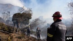 Les équipes de lutte contre les incendies amortissent la végétation couvante, obtenant enfin un feu de forêt féroce sous contrôle sur les contreforts de Table Mountain au Cap le 19 avril 2021.