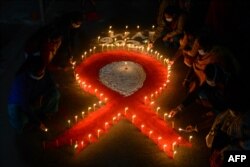 Relawan dan pekerja seks menyalakan lilin berbentuk pita merah pada malam peringatan 'Hari AIDS Sedunia' di kawasan Khalpara di Siliguri, 30 November 2021.(Diptendu DUTTA / AFP)