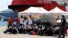 FILE - Migrants sit on the ground after disembarking from Vos Hestia ship of NGO "Save the Children" in the Sicilian harbor of Augusta, Italy, Aug. 4, 2017.