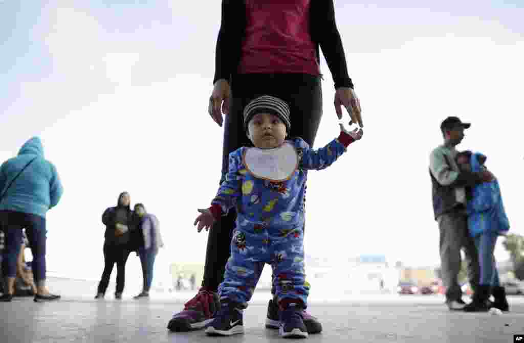 In this June 13, 2018 photo, nine month-old Jesus Alberto Lopez, center, stands with his mother, Perla Murillo, as they wait with other families to request political asylum in the United States, across the border in Tijuana, Mexico. The family, from the Mexican state of Michoacan, has waited for about a week in this Mexican border city, hoping for a chance to escape widespread drug violence at home.