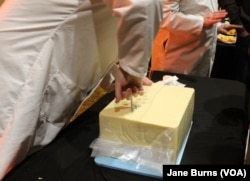 Judges at the U.S. Cheese Championship give visitors to the gala a chance to see how they do their job and to ask questions, in Green Bay, Wis., March 7, 2019. The first step is pulling out a piece of cheese to sample from a 40-pound block of cheddar.