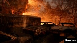 Los fuertes vientos de San Ana soplan las brazas cerca de un auto en llamas cerca de Santa Paula, California.