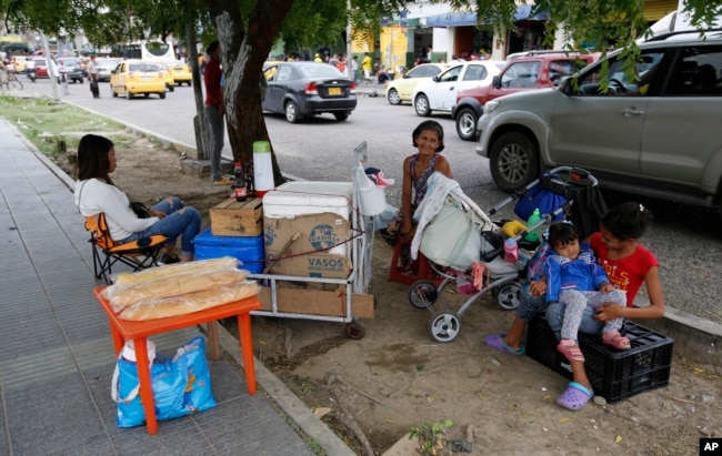 En esta foto del 28 de junio de 2018, la migrante venezolana Maria Fuentes, en el centro, se sienta con su hija, a la izquierda, y dos nietas mientras vende bocadillos en la vereda de Cúcuta, Colombia.