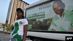 Noël Akossi Bendjo, maire du Plateau, sur une affiche derrière une jeune fille en T-shirt aux couleurs de son parti, à Abidjan, Côte d’Ivoire, 13 avril 2013.