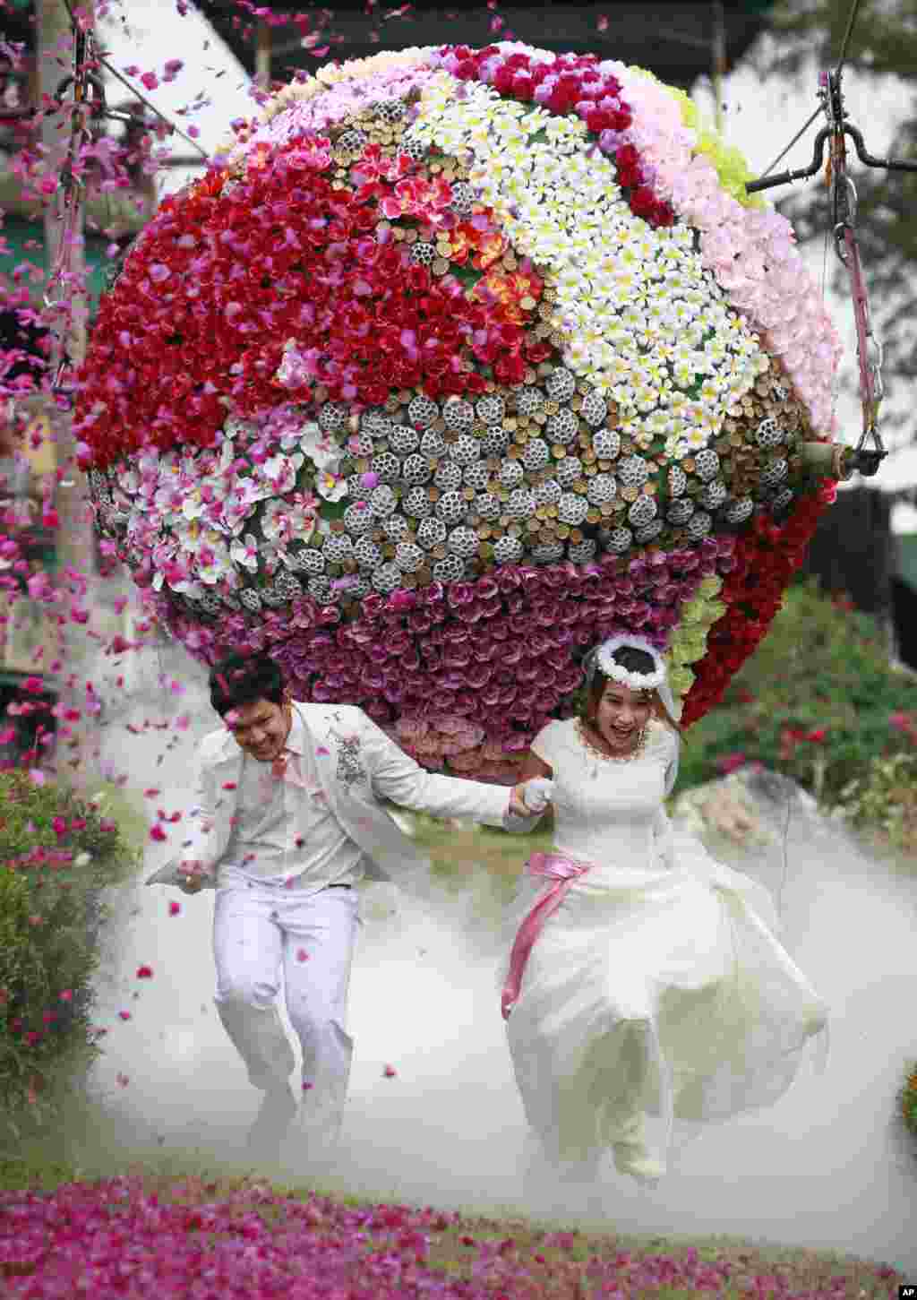 Prasit Rangsitwong, left, and Varutton Rangsitwong run away from a giant flower ball as a part of an adventure-themed wedding ceremony in Prachinburi province, Thailand, on the eve of Valentine&#39;s Day.