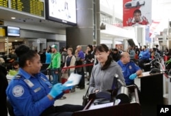 FILE - A TSA officer, left, checks a passenger's ticket, boarding pass and passport as part of security screening at John F. Kennedy International Airport.