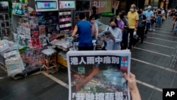 FILE - A woman tries to take a picture of last issue of Apple Daily in front of a newspaper stand as people queue to buy the issue at a downtown street in Hong Kong, June 24, 2021. 