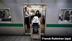 Tomomi Ota pulls a cart loaded with her humanoid robot Pepper as she boards a subway train in Tokyo, Japan, 27 June 2016.