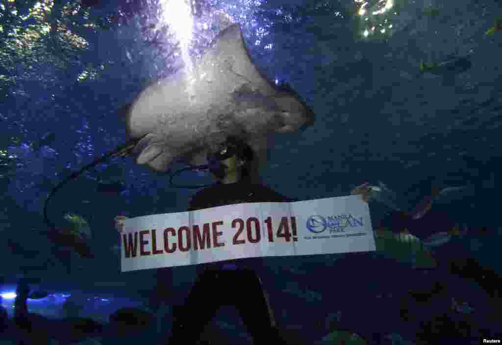 Seorang penyelam profesional memegang spanduk &quot;Welcome 2014&quot; saat berenang di sebelah ikan pari pada perayaan malam tahun baru di dalam akuarium besar di sebuah taman laut di Manila, Filipina (31/12). (Reuters/Romeo Ranoco)