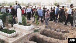 Mourners walk past open graves during a funeral for four people killed in a government raid on a Damascus neighborhood Thursday