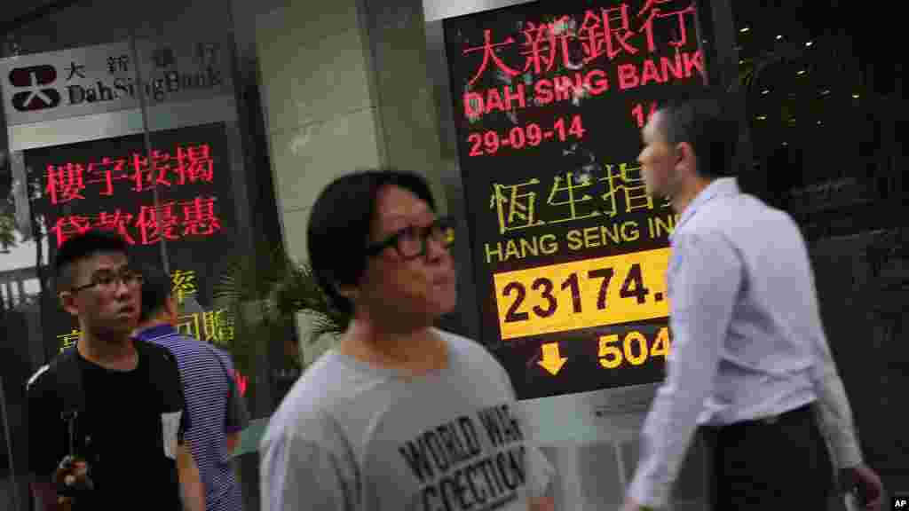 People walk past an electronic ticker showing Hong Kong's benchmark Hang Seng Index dropping more than 500 points soon after opening in Hong Kong, Sept. 29, 2014.