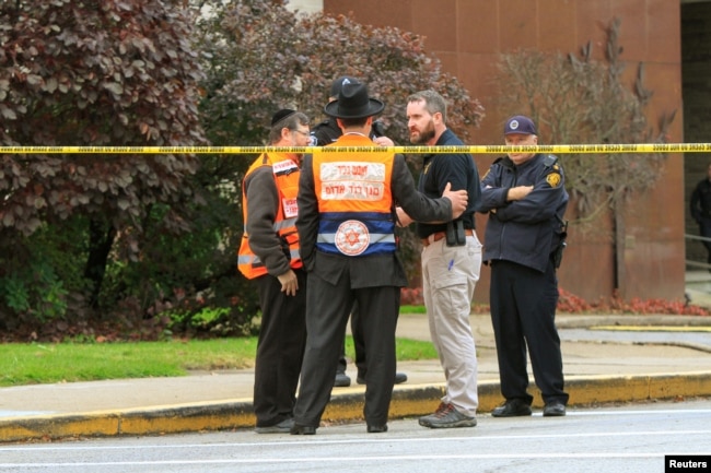 Police officers guarding the Tree of Life Synagogue following a shooting there speak with men in orange vests from a Jewish burial society in Pittsburgh, Pa., Oct. 27, 2018.