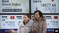 Woman walk past an electronic stock board showing Japan's Nikkei 225, top right, and Hong Kong's Hang Seng, bottom left, at a securities firm in Tokyo, Jan. 20, 2016. 