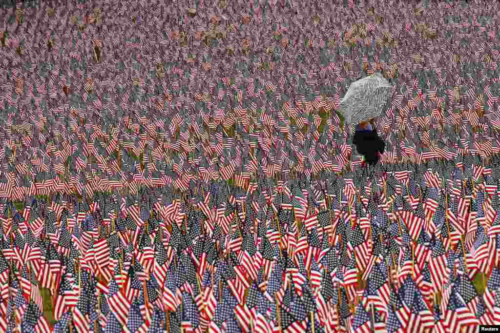 A pedestrian carrying an umbrella walks through a Memorial Day display of United States flags on the Boston Common in Boston, Massachusetts. 