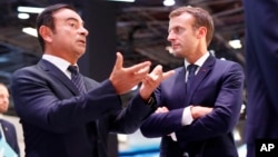 French President Emmanuel Macron listens to Carlos Ghosn, the CEO of French car maker Renault, left, at the Renault stand during an official visit at the Paris Motor Show, in Paris, France, Oct. 3, 2018.