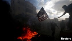 A Palestinian protester prepares to burn a U.S. flag during clashes with Israeli troops at a protest against U.S. President Donald Trump's decision to recognize Jerusalem as the capital of Israel, near the Jewish settlement of Beit El, near the West Bank