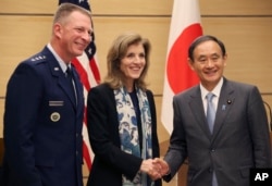 FILE - U.S. Ambassador to Japan Caroline Kennedy, center, accompanied by Lt. Gen. John Dolan, left, commander of U.S. Forces Japan, shakes hands with Japanese Chief Cabinet Secretary Yoshihide Suga after a joint press conference in Tokyo.
