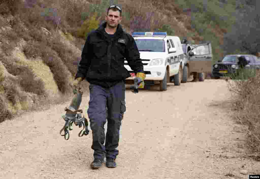 An Israeli police explosive expert carries the remains of a rocket after it landed near the northern town of Kiryat Shmona, Israel, Dec. 29, 2013.&nbsp;