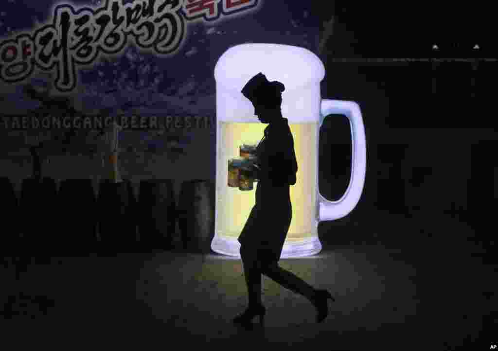 A waitress is silhouetted against an advertisement board as she carries jugs of beer during Taedonggang Beer Festival in Pyongyang, North Korea.