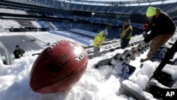 A football with the Super Bowl XLVIII logo is set on a mound of snow as workers shovel snow off the seating area at MetLife Stadium as crews removed snow ahead of Super Bowl XLVIII following a snow storm, Jan. 22, 2014, in East Rutherford, New Jersey.