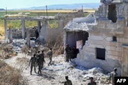 Syrian regime forces gather near a damaged building at the entrance of the town Kafr Nabouda, in the north of the Syrian Hama province, May 26, 2019.