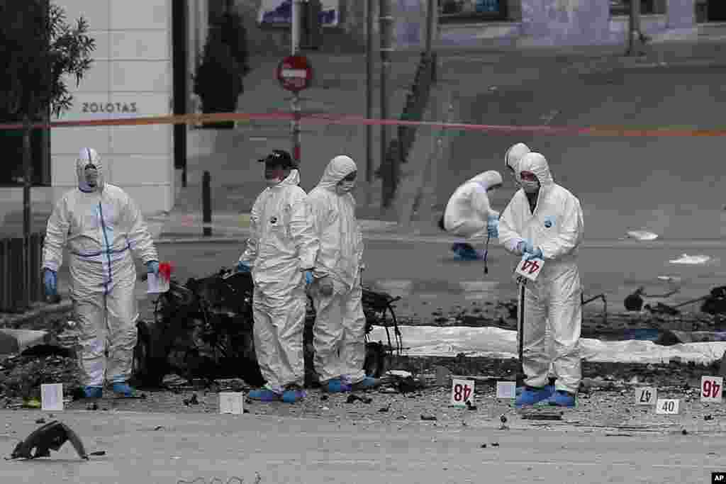 Police bomb disposal experts search for evidence next to the remains of a car after a car bomb explosion in central Athens, Greece. A bomb exploded outside a Bank of Greece building before dawn, causing some damage but no injuries.