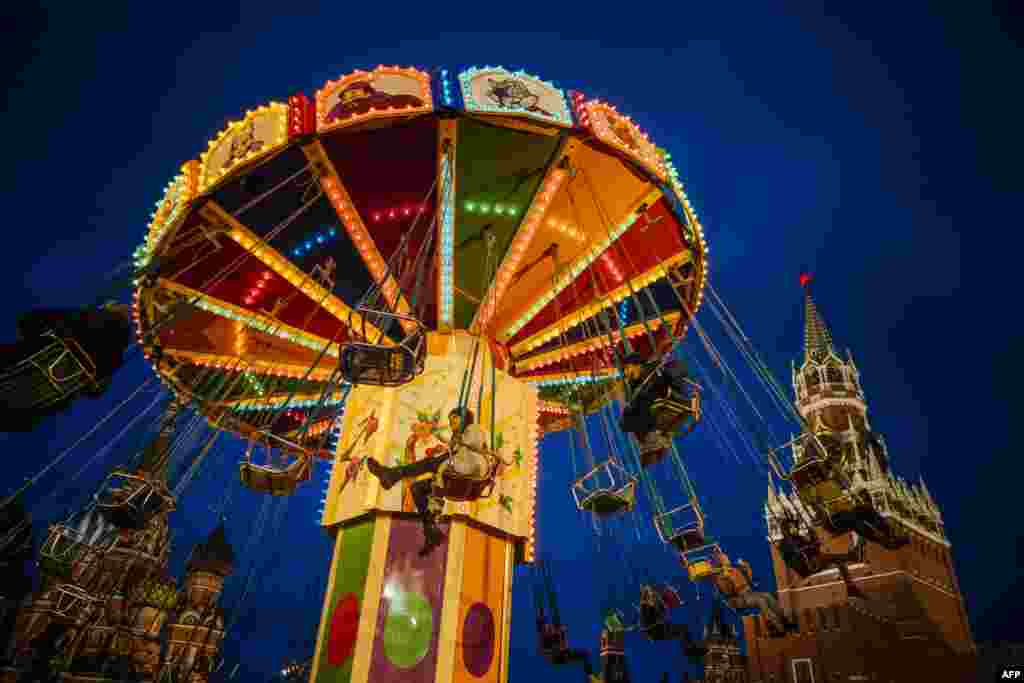 People ride a merry-go-round at the Christmas Market at the Red Square in Moscow, Russia, as the Kremlin&#39;s Spasskaya Tower is seen in the background on December 16, 2019.