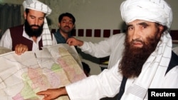 Jalaluddin Haqqani (R), the Taliban's Minister for Tribal Affairs, points to a map of Afghanistan during a visit to Islamabad, Pakistan while his son Naziruddin (L) looks on in this October 19, 2001 file photograph. 