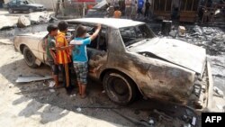 Iraqi children inspect a burned out car at the site of a car bomb attack that exploded the previous day in a commercial street of Baghdad's eastern neighborhood of Mashtal, Sept.16, 2013.