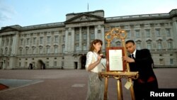 La secretaria de prensa de la Reina Isabel II, Ailsa Anderson, y el ahora exempleado del Palacio Real, Badar Azim, al momento de colocar el documento que ceritifca el nacimiento del príncipe de Cambridge.