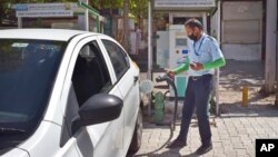 FILE - A driver of an electric car charges his vehicle at public charging station in New Delhi, India, April 1, 2021. 