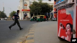 An Indian pedestrian crosses a road near roadside kiosk with a Coca-cola advertisement in New Delhi, India, Feb. 12, 2016. Coca-Cola suspended bottling at three plants in India, including one in the parched northwest where farmers have been protesting the company's use of dwindling groundwater reserves.