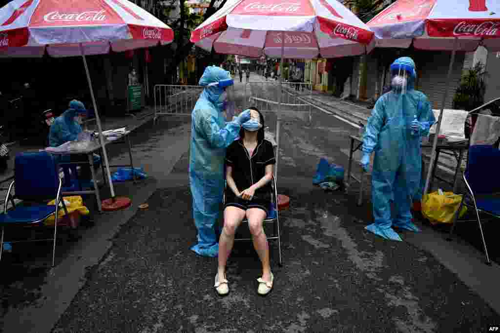 A healthcare worker wearing personal protective equipment (PPE) collects cells from the nose of a woman (C) for COVID-19 testing in the Old Quarter of Hanoi, Vietnam.