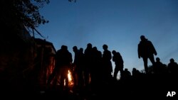 Para migran menghangatkan diri dekat api unggun sementara menunggu masuk ke kamp di Spielfeld, Austria (25/10). (AP/Petr David Josek)