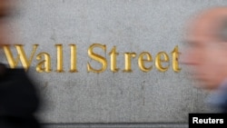 FILE - People walk by a Wall Street sign close to the New York Stock Exchange in New York.