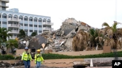 Workers walk past the collapsed and subsequently demolished Champlain Towers South condominium building, Tuesday, July 6, 2021, in Surfside, Fla. (AP Photo/Lynne Sladky)