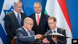 Staying on a four-day official visit in Hungary, Israeli Prime Minister Benjamin Netanyahu, rear left, and his Hungarian counterpart Viktor Orban, rear right, look on as Israeli Ambassador Yosef Amrani, left, and Hungarian Minister of National Economy Mihaly Varga sign a declaration on cooperation in the field of innovation between the two countries in the Parliament building in Budapest, Hungary, July 18, 2017.