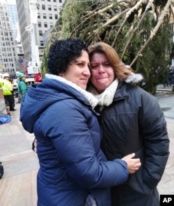 Lissette Gutierrez, left, hugs her wife, Shirley Figueroa, with the 72-foot-tall Norway spruce that the couple donated in the background, Nov. 10, 2018 in New York.
